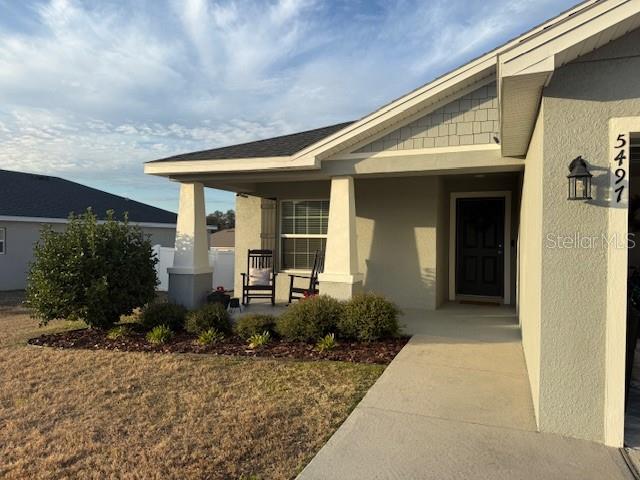 A single-story house exterior features a covered front porch, two rocking chairs, and landscaping — 5497 SE 91ST PLACE, OCALA, FL