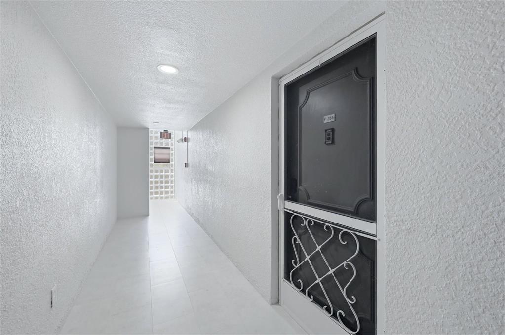 A white hallway leads to a door with a decorative metal screen and number 205 — 2100 BENJAMIN FRANKLIN DRIVE UNIT 205, SARASOTA, FL