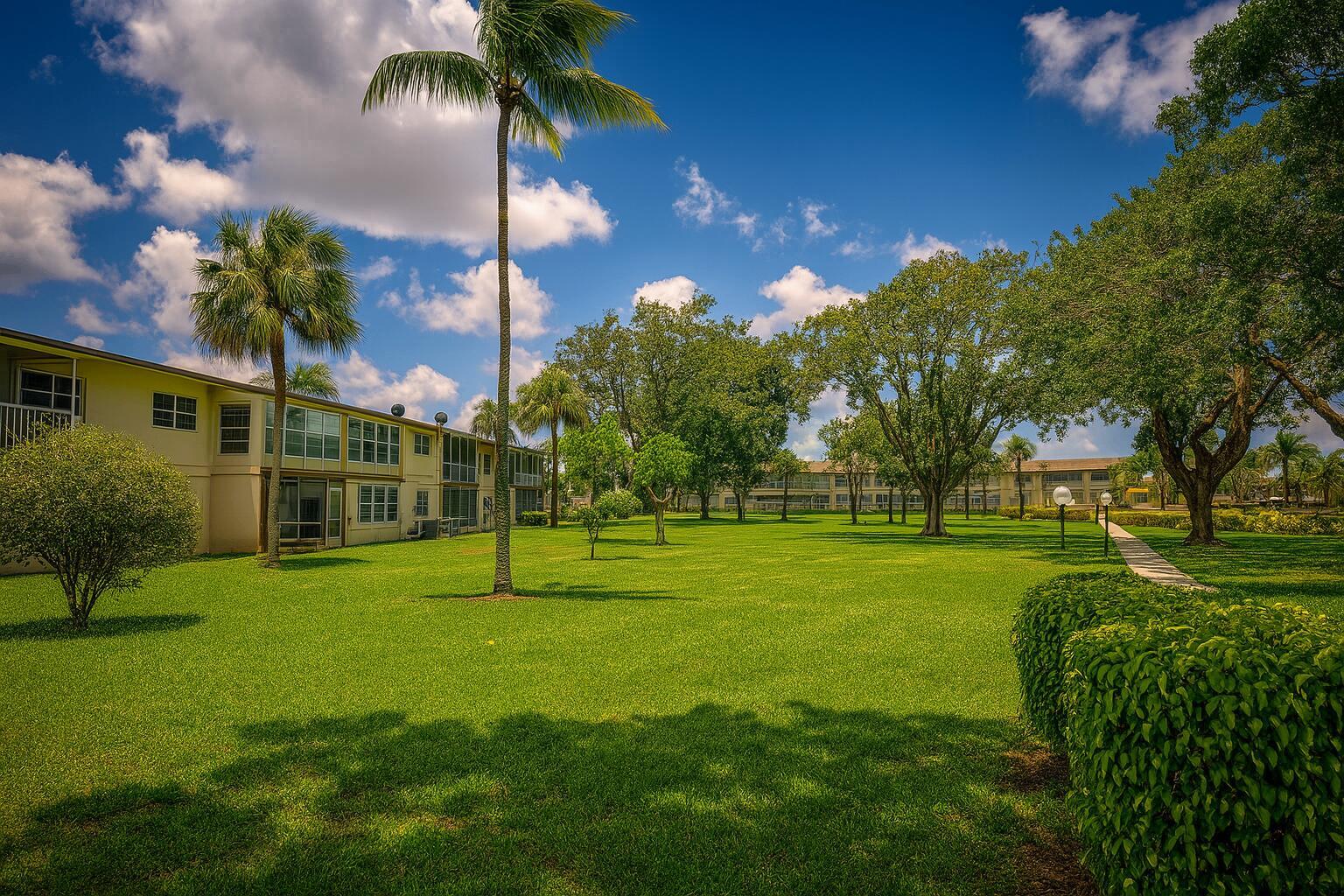 A grassy courtyard with palm trees and large shade trees between two-story apartment buildings — 550 NW 78th Terrace # 107, Margate FL 33063, MARGATE, FL