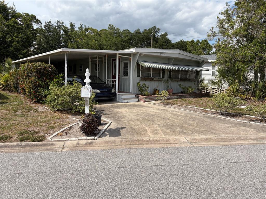 A single-story manufactured home with a carport, driveway, and a white mailbox in front — 1451 BURNING TREE STREET, SARASOTA, FL