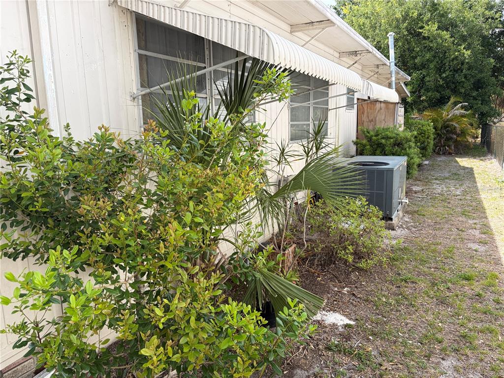 The exterior side of a mobile home features metal awnings, landscaping, and an air conditioner — 1451 BURNING TREE STREET, SARASOTA, FL