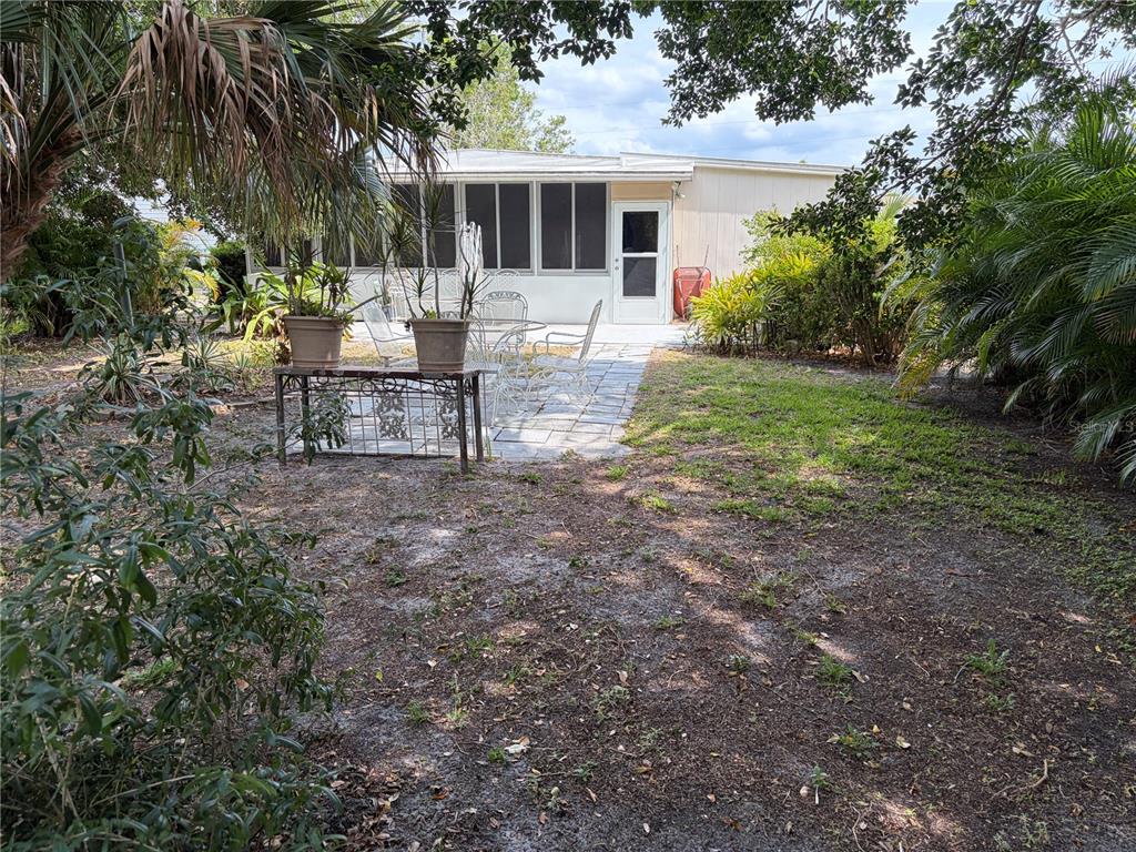 A patio with metal furniture sits in front of a house with a screened porch — 1451 BURNING TREE STREET, SARASOTA, FL