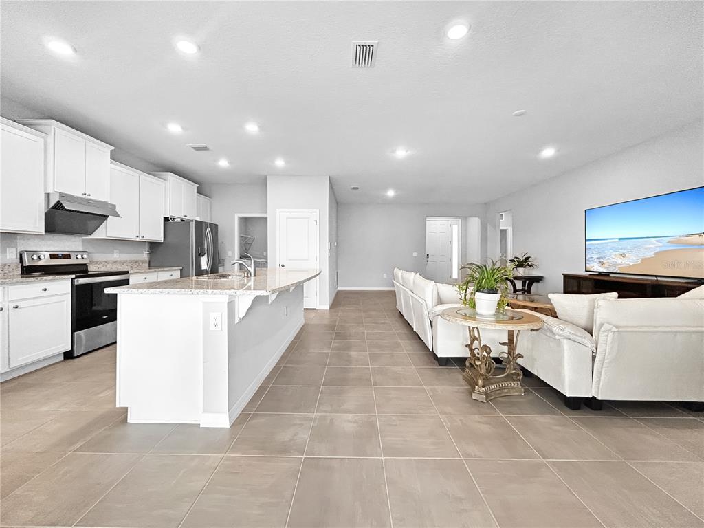 An open-concept kitchen and living area feature white cabinetry, granite countertops, and tile flooring — 503 158TH STREET E, BRADENTON, FL