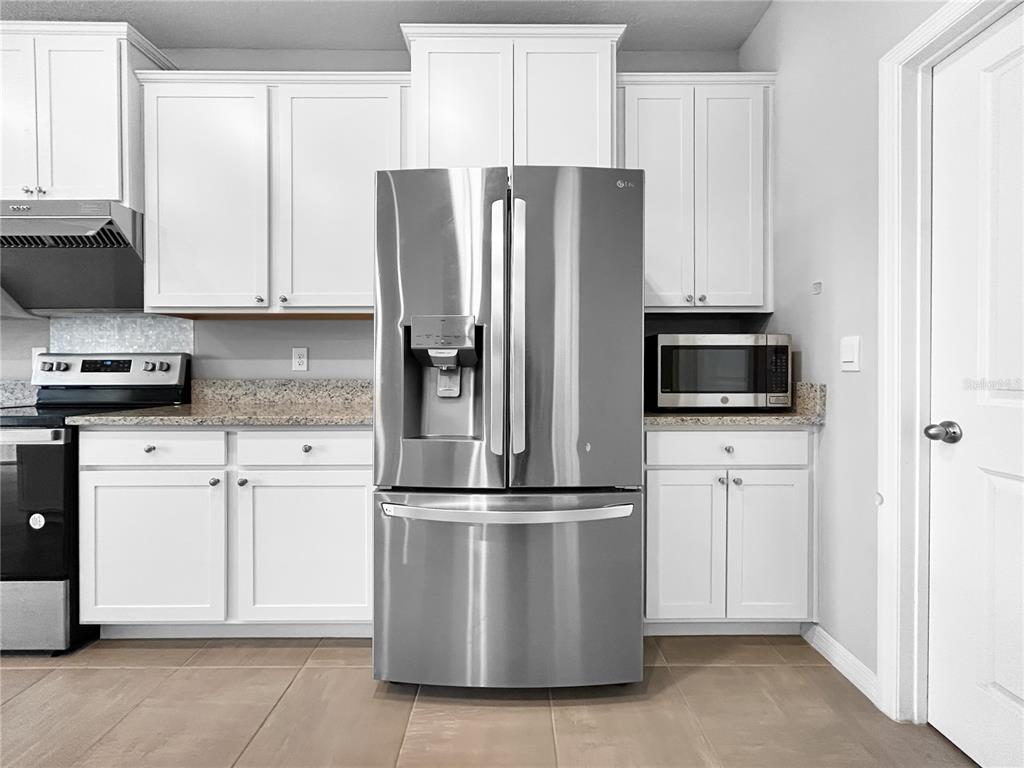 A kitchen features white cabinets, granite countertops, stainless steel appliances, and tile flooring — 503 158TH STREET E, BRADENTON, FL