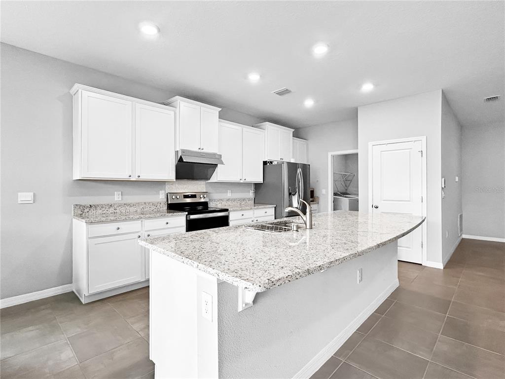 A modern kitchen features white cabinets, granite countertops, a central island, and stainless steel appliances — 503 158TH STREET E, BRADENTON, FL