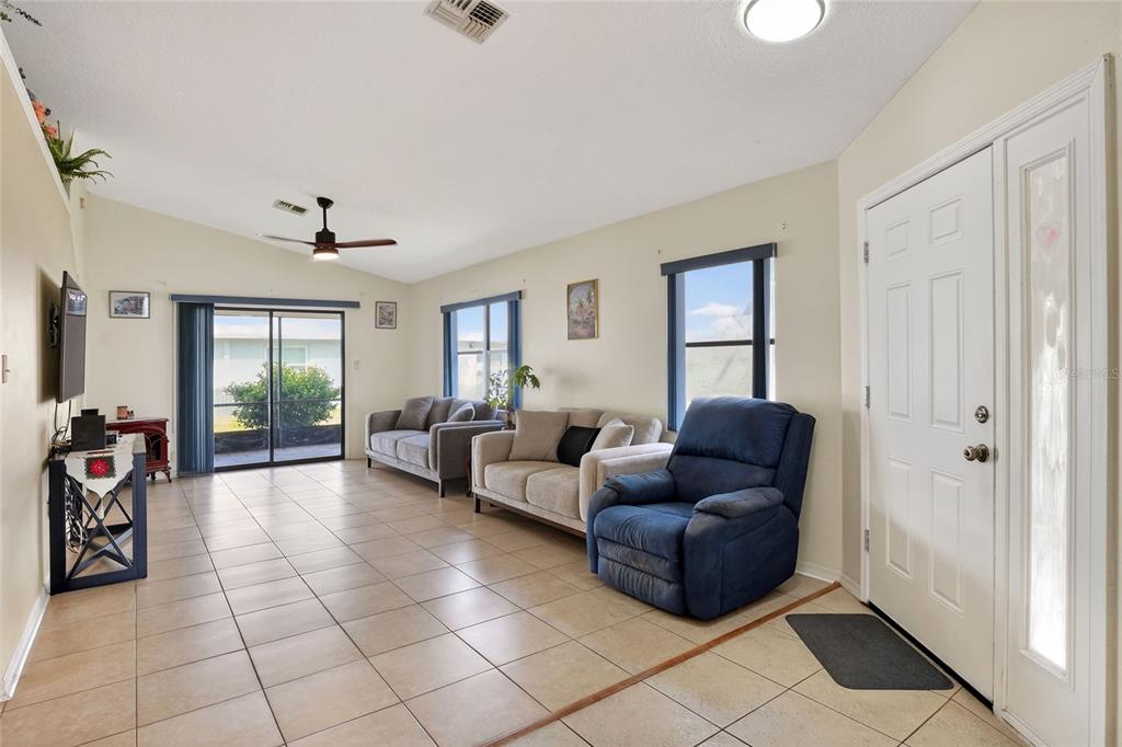 A living room features tile flooring, a ceiling fan, a sliding glass door, and furniture — 6264 PEACOCK RUN, LAKELAND, FL