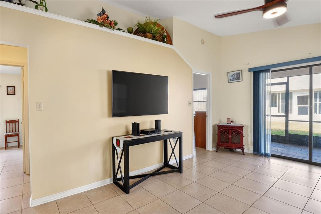 A living room features a wall-mounted television, a console table, and a sliding glass door — 6264 PEACOCK RUN, LAKELAND, FL