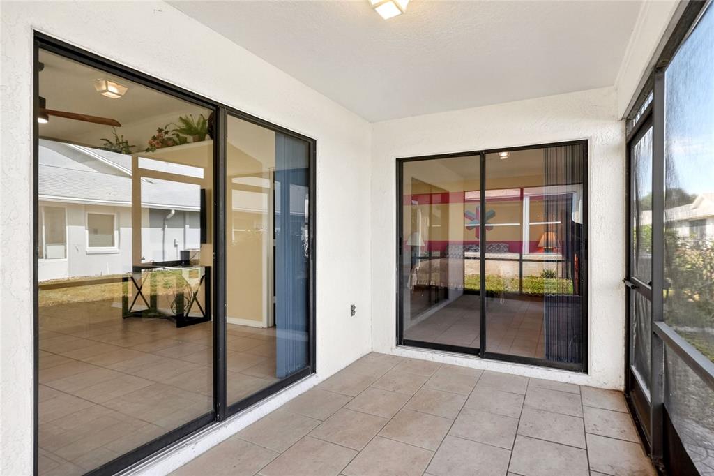 A covered patio with tiled flooring and two sliding glass doors leading into the home — 6264 PEACOCK RUN, LAKELAND, FL