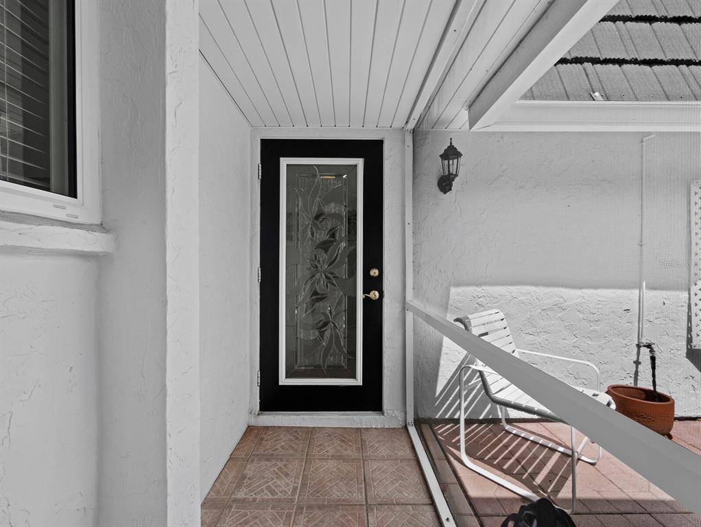A covered patio features a black door with a decorative glass insert and tiled flooring — 3828 BLUE STONE WAY UNIT 77, SARASOTA, FL