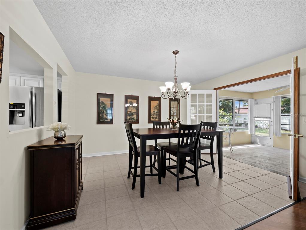 A dining room with tile floors, a dark wood table, and a view into a sunroom — 3828 BLUE STONE WAY UNIT 77, SARASOTA, FL