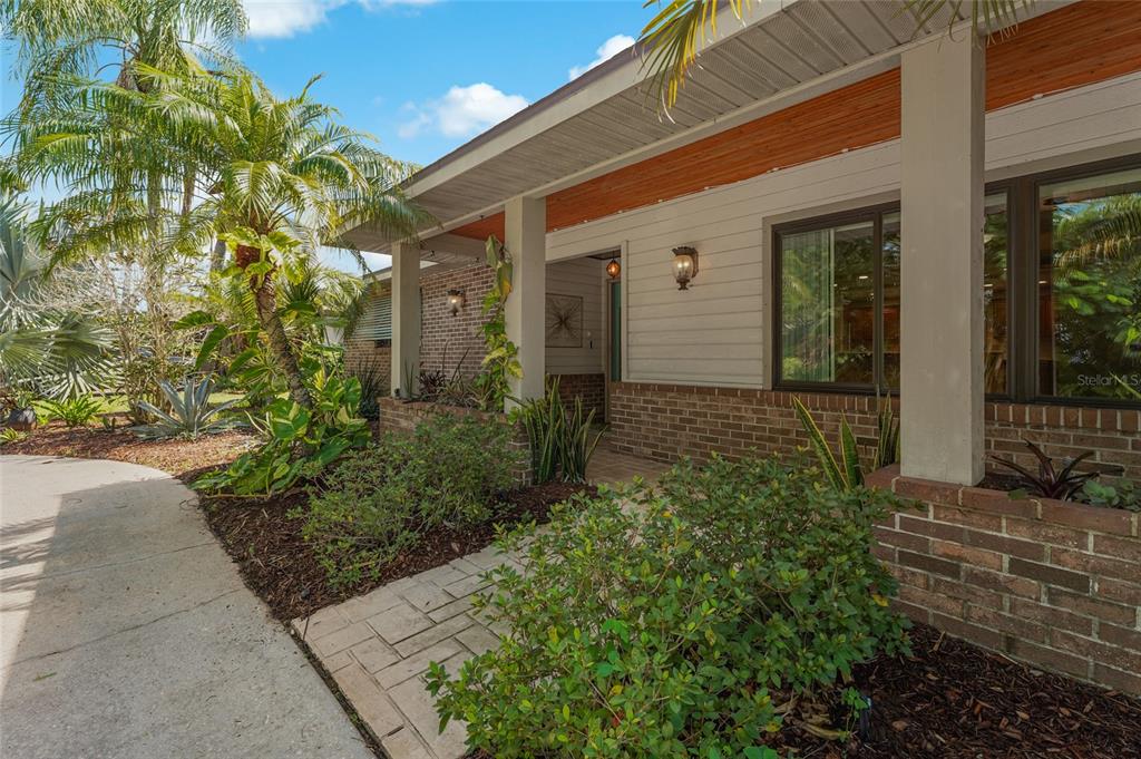 A brick and horizontal siding house exterior features a covered porch and tropical landscaping — 3781 COUNTRYSIDE ROAD, SARASOTA, FL