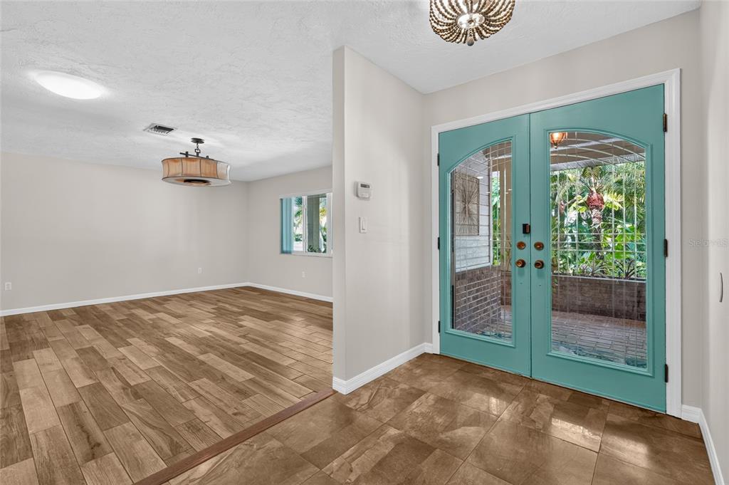 An entryway with tile flooring leads to a living area featuring wood-look floors and double doors — 3781 COUNTRYSIDE ROAD, SARASOTA, FL
