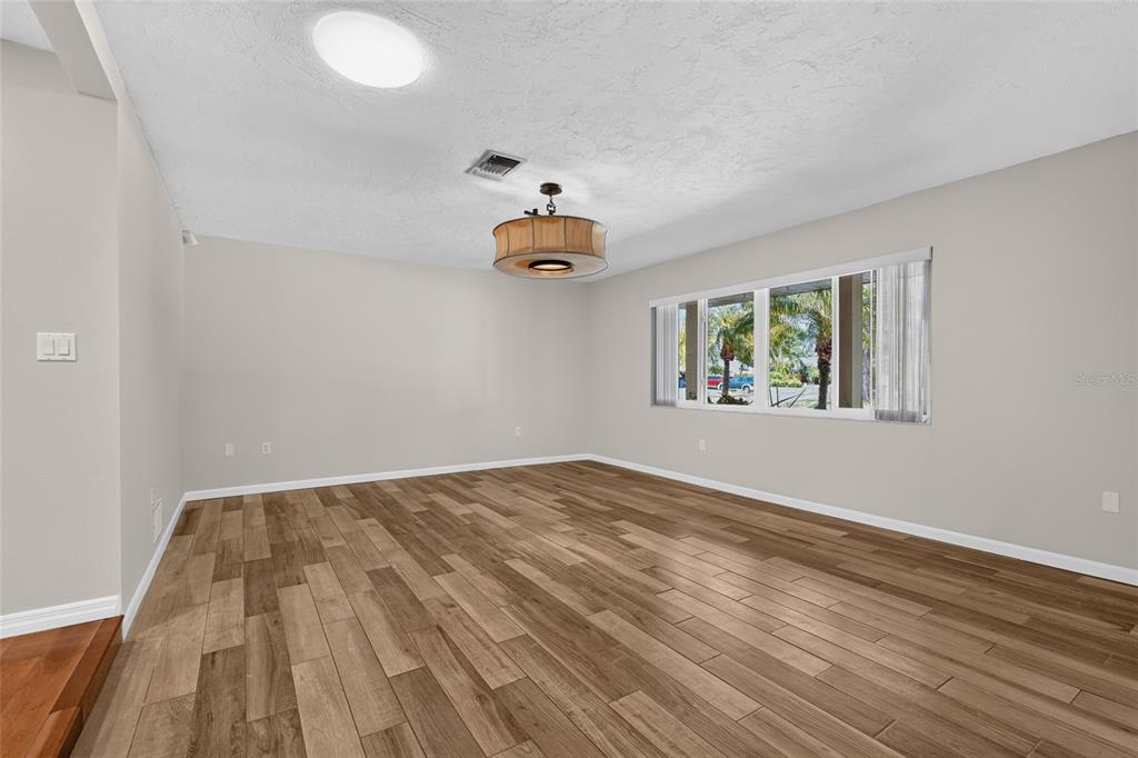 An empty room features wood-look tile flooring, a drum pendant light, and a large window — 3781 COUNTRYSIDE ROAD, SARASOTA, FL
