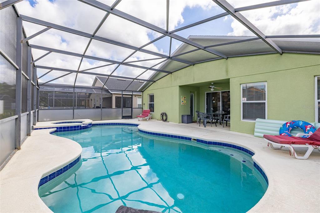 A screened-in swimming pool and hot tub sit on a patio behind a green house — 756 SCRUB JAY WAY, DAVENPORT, FL