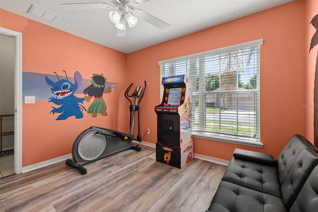 A room with orange walls, wood-look flooring, an elliptical machine, an arcade cabinet, and sofa — 756 SCRUB JAY WAY, DAVENPORT, FL