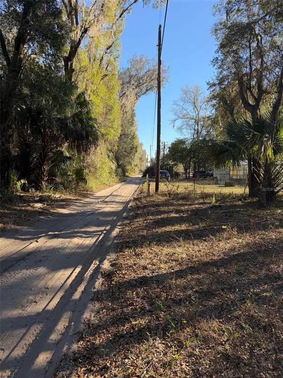 A dirt road runs alongside a wooded area with a utility pole and nearby structures — TBD NE 150 AVENUE, FORT MC COY, FL