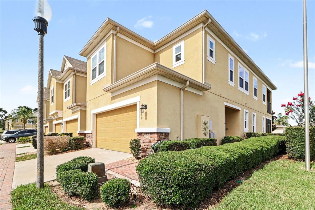 A two-story tan stucco townhouse with a garage and manicured hedges in front — 13500 FOUNTAINBLEAU DRIVE, CLERMONT, FL