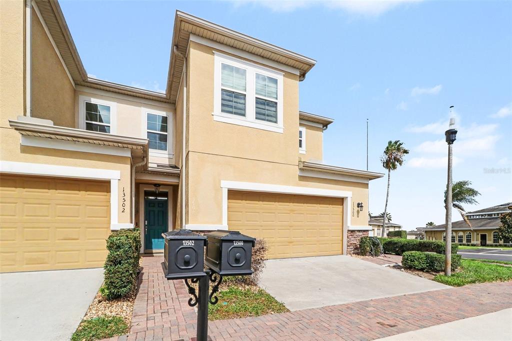 A two-story tan stucco townhouse features a two-car garage and a front-facing mailbox post — 13500 FOUNTAINBLEAU DRIVE, CLERMONT, FL