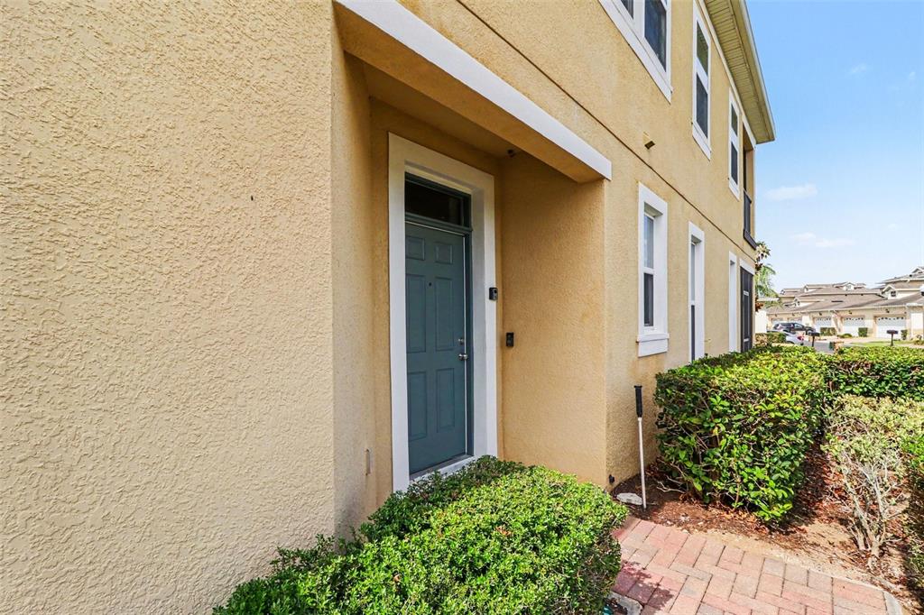 A tan stucco building exterior features a blue front door and a brick walkway — 13500 FOUNTAINBLEAU DRIVE, CLERMONT, FL