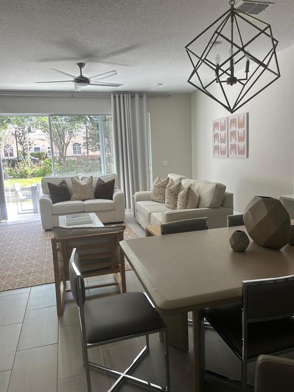 An open-concept living and dining area features tile floors, a geometric chandelier, and patio access — 7813 SPECTRUM DRIVE, REUNION, FL