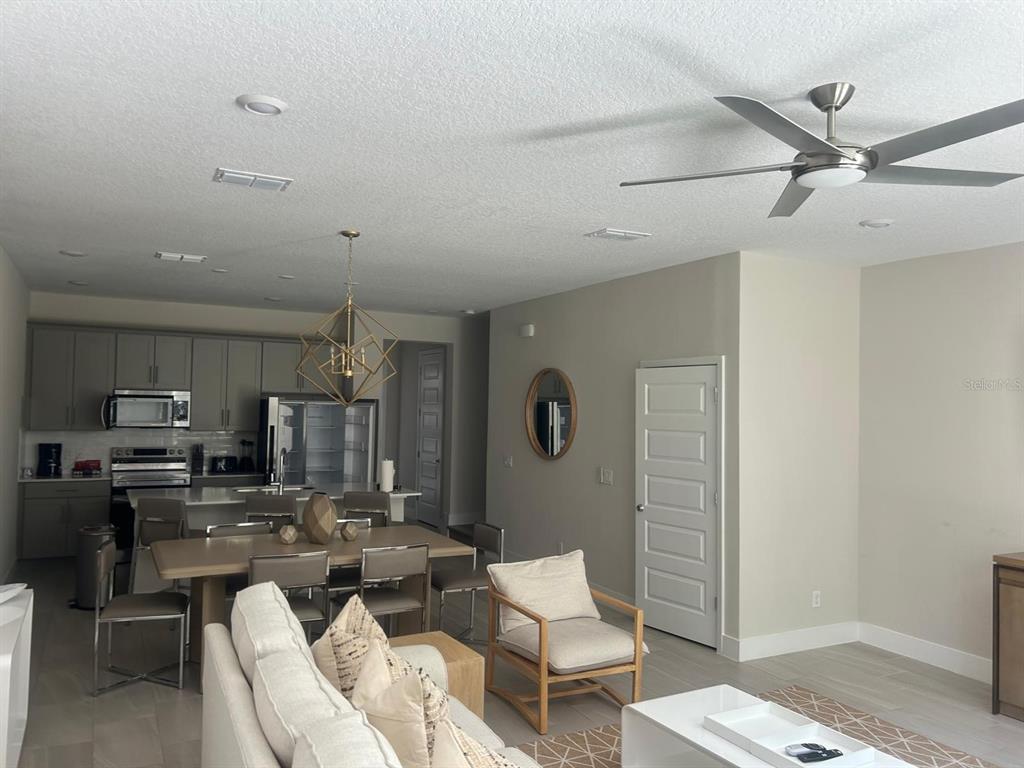 An open-concept living and dining area features a modern kitchen, light flooring, and a ceiling fan — 7813 SPECTRUM DRIVE, REUNION, FL
