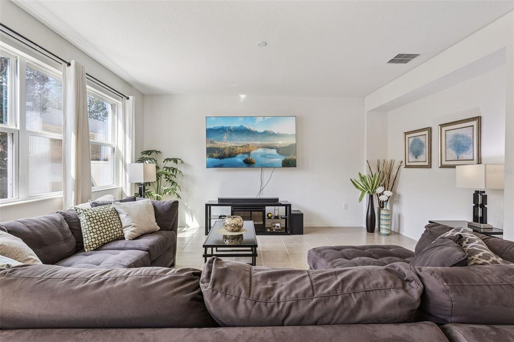 A living room features a large sectional sofa, a wall-mounted television, and tile flooring — 11437 WISHING WELL LANE, CLERMONT, FL