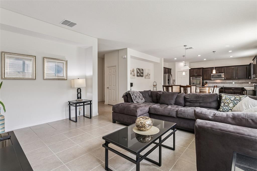 A living room with tile flooring, a large sectional sofa, and an open-concept kitchen — 11437 WISHING WELL LANE, CLERMONT, FL