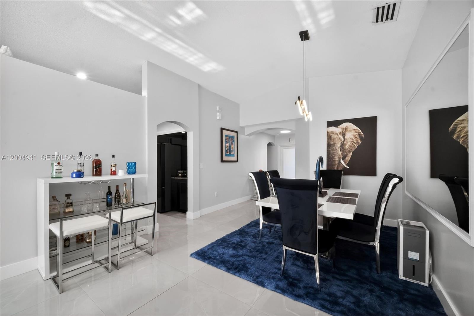 A dining room features a white table, black chairs, a blue rug, and a bar area — 14471 SW 136th Pl, Miami FL 33186, MIAMI, FL