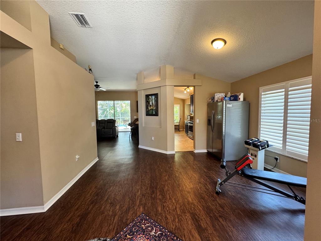 A living area with wood-look flooring, a workout bench, and a view into the kitchen — 6207 TUPELO TRAIL, LAKEWOOD RANCH, FL