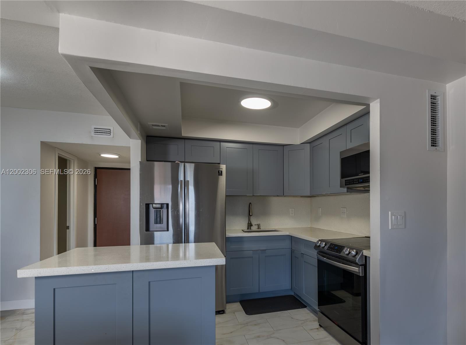 A kitchen features blue cabinets, stainless steel appliances, and a white quartz countertop island — 300 NW 42nd Ave # 610, Miami FL 33126, MIAMI, FL