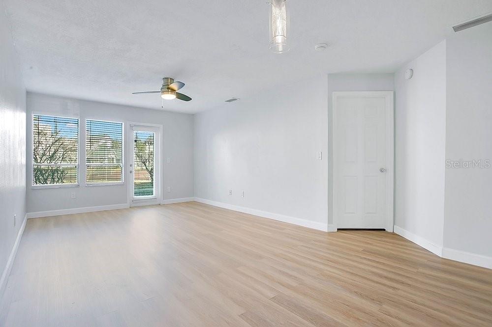 An empty living room features light-colored wood-look flooring, white walls, and a ceiling fan — 9513 DARIEN AVENUE UNIT 9513, ORLANDO, FL