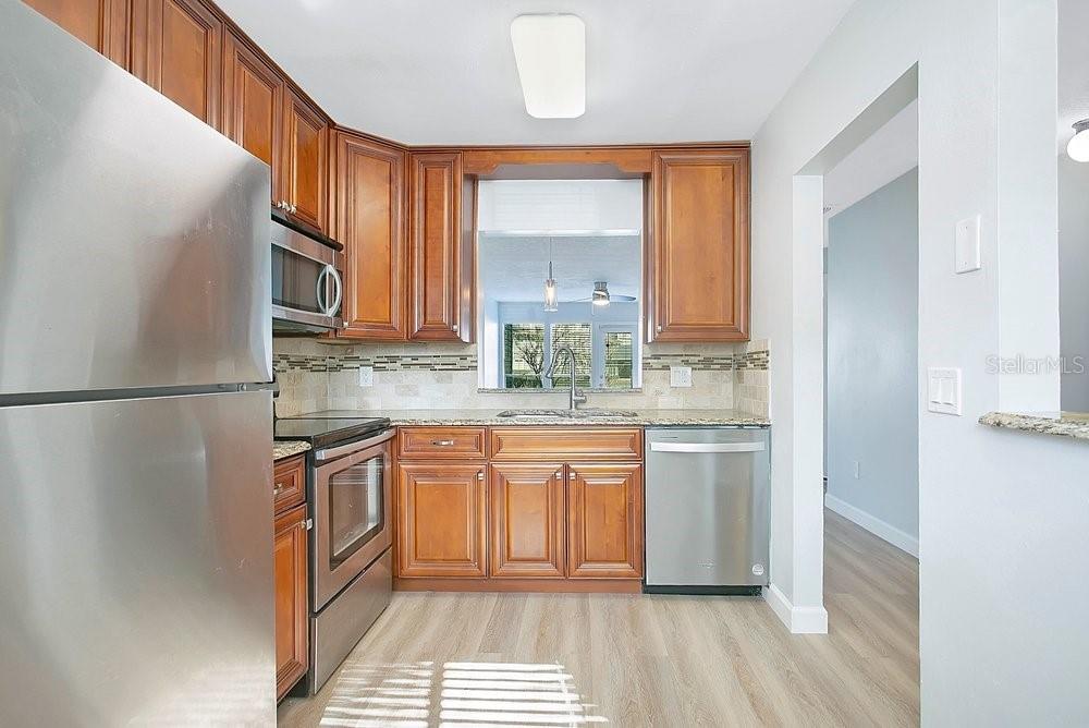 A kitchen features wood cabinets, stainless steel appliances, granite countertops, and light-colored wood flooring — 9513 DARIEN AVENUE UNIT 9513, ORLANDO, FL