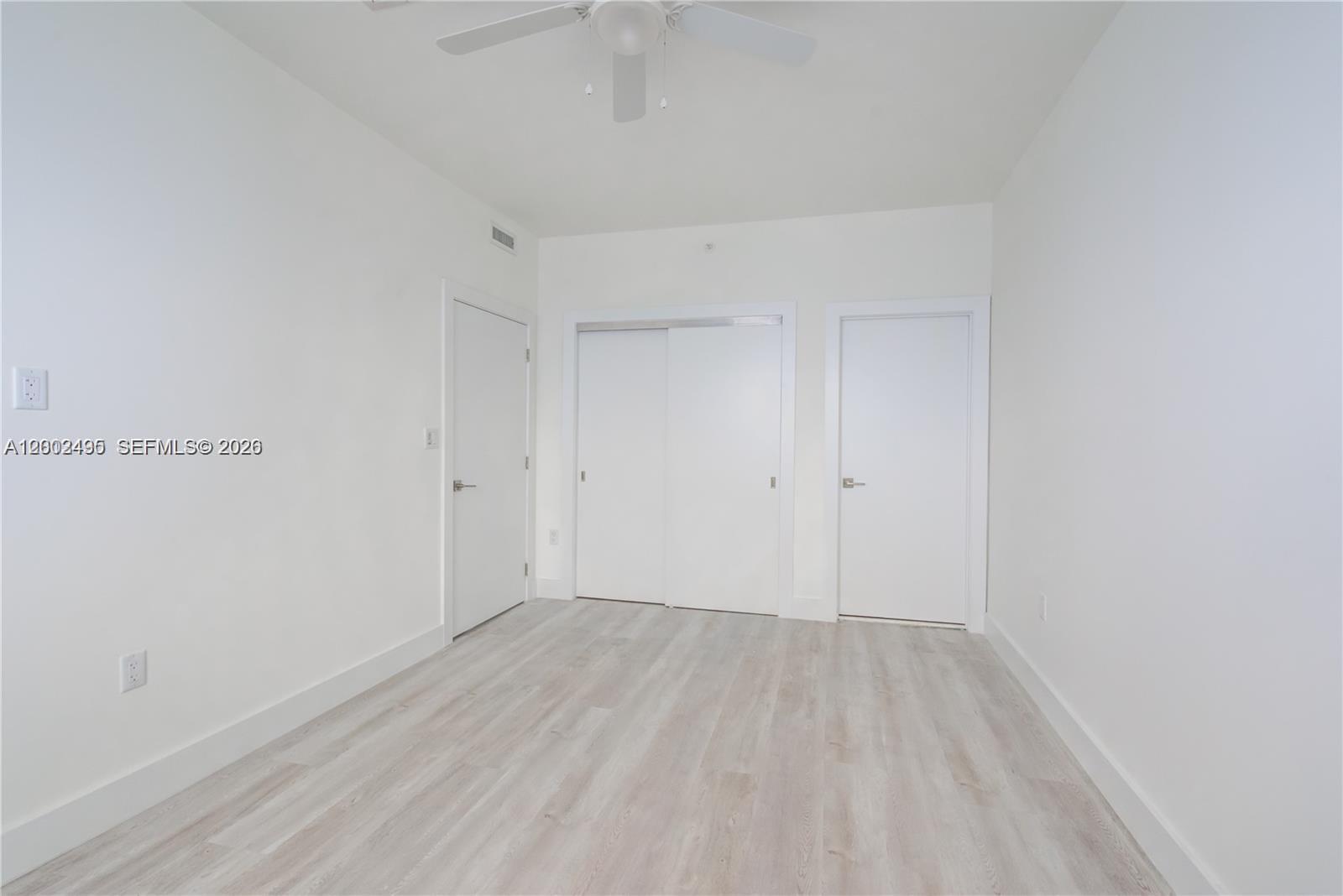 An empty room features white walls, light wood-look flooring, a ceiling fan, and three doors — 940 Michigan Ave # 4, Miami Beach FL 33139, MIAMI BEACH, FL