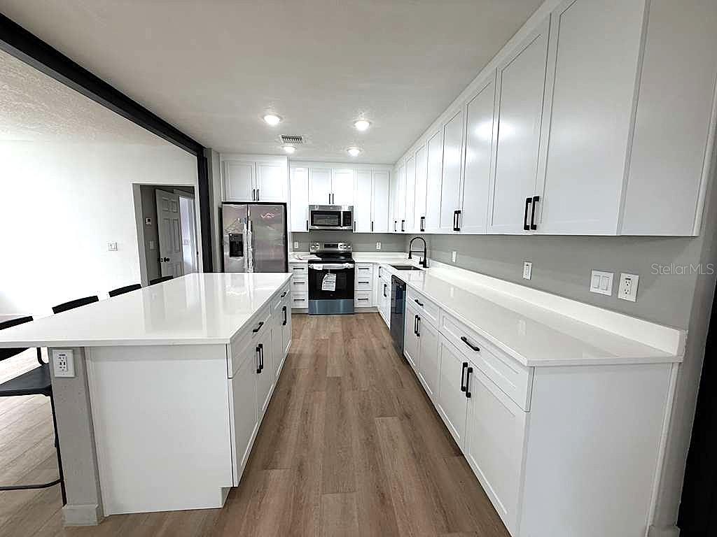 A modern kitchen features white cabinetry, quartz countertops, stainless steel appliances, and wood-look flooring — 1741 LYNDALE BOULEVARD, MAITLAND, FL