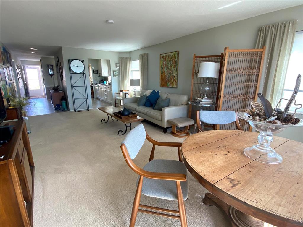 A living and dining area features beige carpet, a light-colored sofa, and a round wooden table — 500 THE ESPLANADE N UNIT 405, VENICE, FL