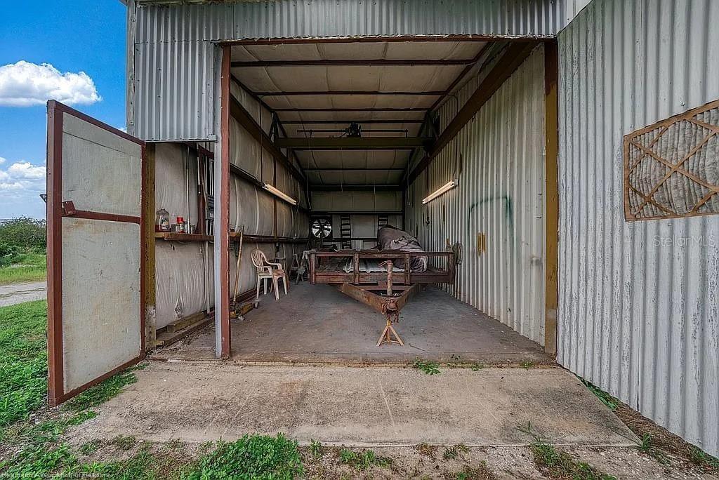 An open-sided metal storage building contains a utility trailer and a plastic chair — 115 HEINLEY ROAD, LAKE PLACID, FL