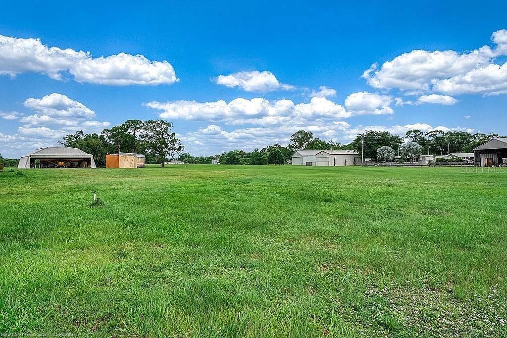 A wide, grassy field features a hangar, a small shed, and a large metal building — 115 HEINLEY ROAD, LAKE PLACID, FL