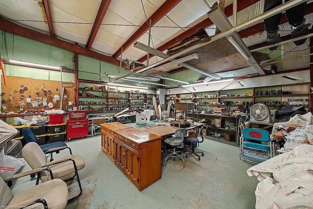A large workshop with exposed metal beams, shelving units, workbenches, and various tools and furniture — 115 HEINLEY ROAD, LAKE PLACID, FL