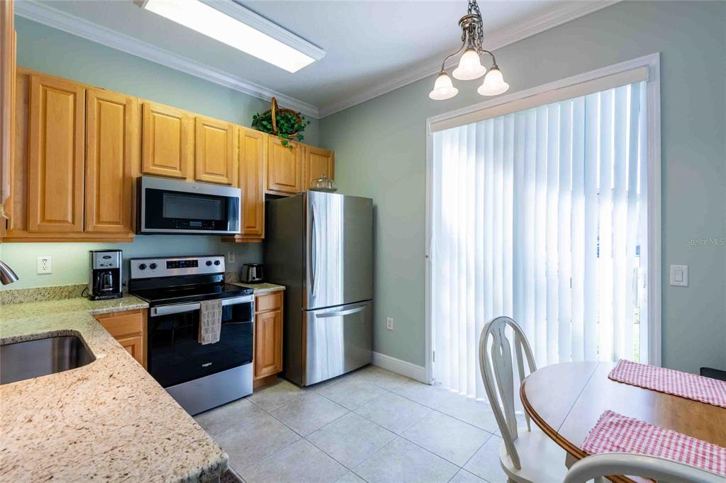 A kitchen features light wood cabinets, stainless steel appliances, granite countertops, and a dining area — 21011 PICASSO COURT UNIT 106, LAND O LAKES, FL