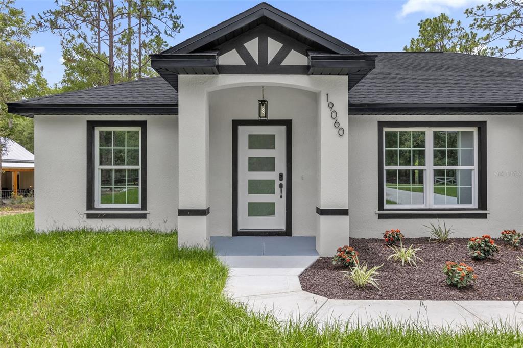 A single-story house with white stucco walls, black trim, and a central front entrance — 19060 SW 57TH PL, DUNNELLON, FL