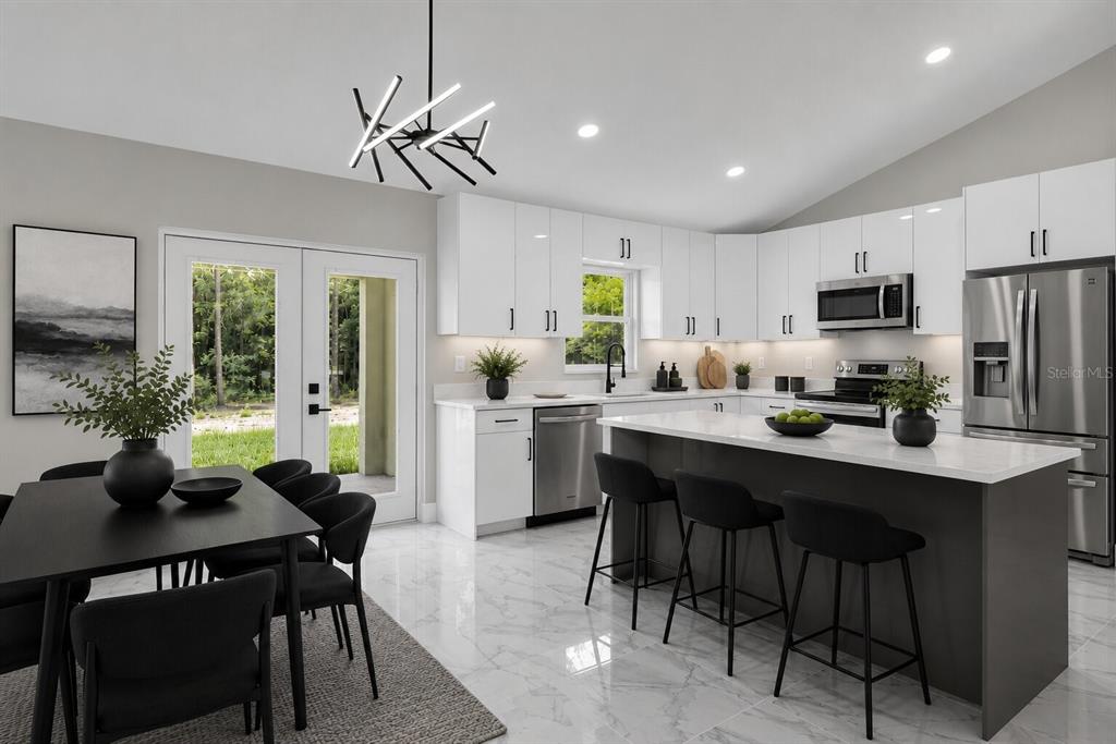 A modern kitchen and dining area features white cabinetry, a dark island, and marble flooring — 19060 SW 57TH PL, DUNNELLON, FL