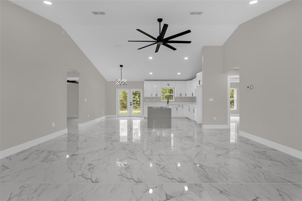 A bright, open-concept kitchen and living area features white cabinetry, a center island, and marble-look tile flooring — 19060 SW 57TH PL, DUNNELLON, FL