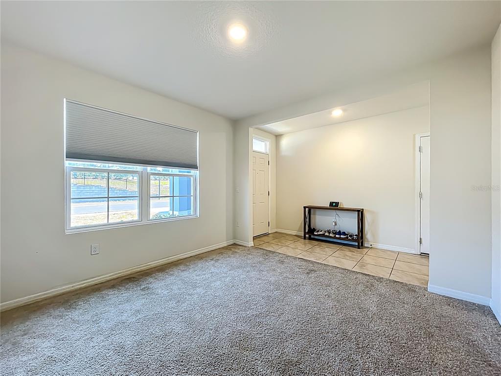 A room with carpeted flooring, a large window, and a tiled entryway with a console table — 3196 BLUE CRAB DRIVE, TAVARES, FL