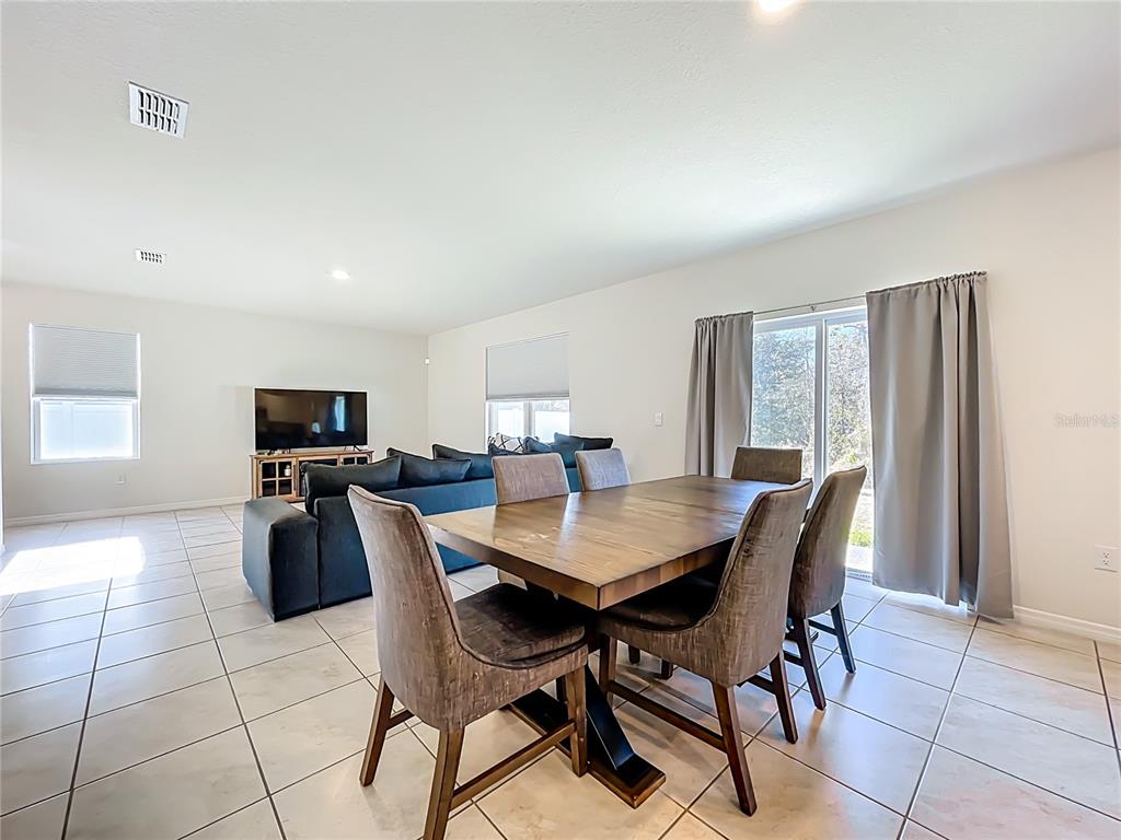 An open-concept living and dining area features tile flooring, a dark sofa, and a wooden table — 3196 BLUE CRAB DRIVE, TAVARES, FL