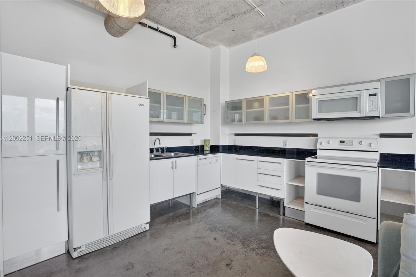 A kitchen features white cabinetry, black countertops, stainless steel appliances, and an exposed concrete ceiling — 10 SW South River Dr # 1410, Miami FL 33130, MIAMI, FL