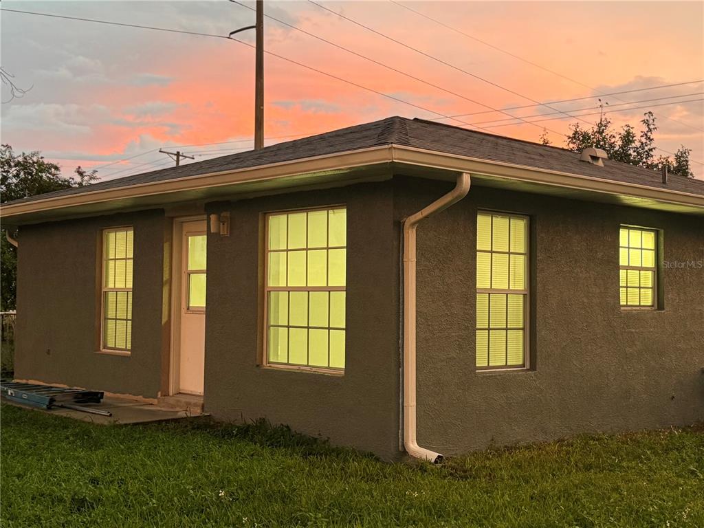 Exterior view of a small, gray stucco house with a hip roof at sunset — 37209 LOCK STREET, DADE CITY, FL
