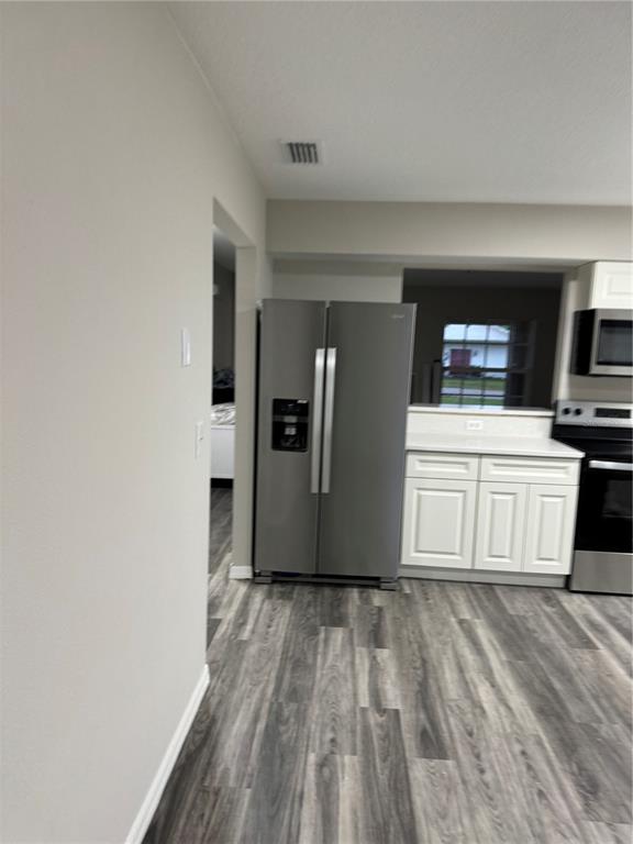 A kitchen features a stainless steel refrigerator, white cabinets, and gray wood-look flooring — 37209 LOCK STREET, DADE CITY, FL
