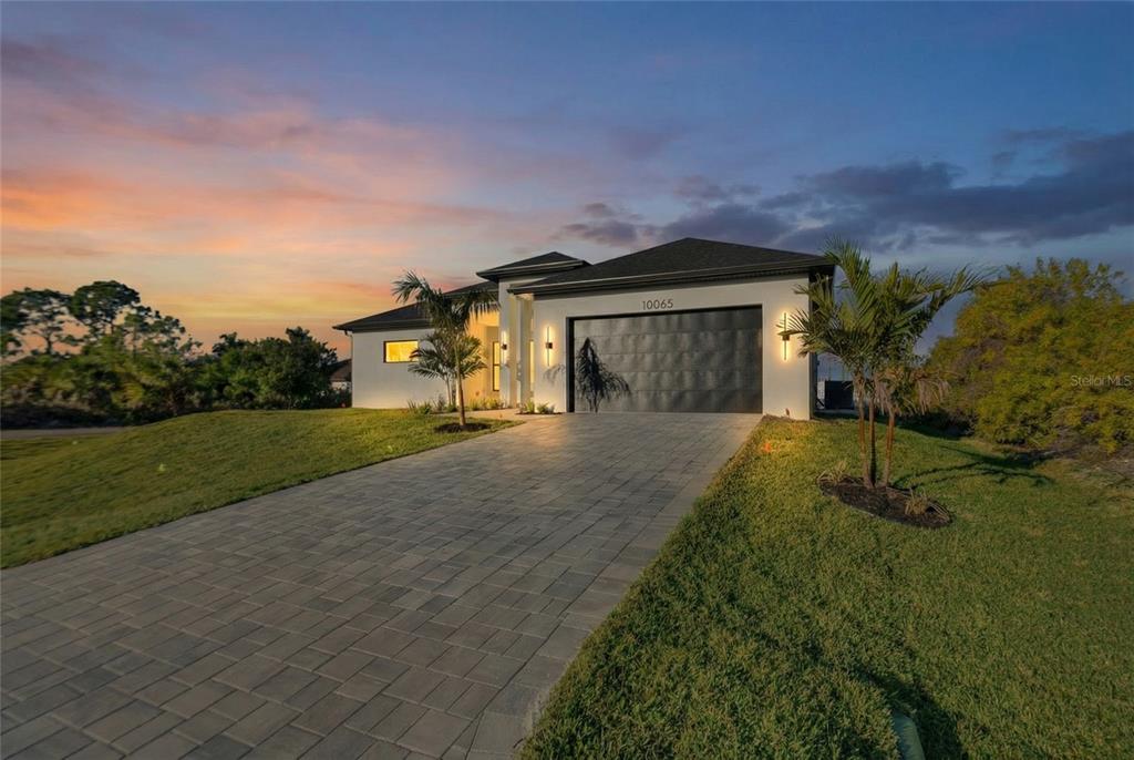 A modern single-story house exterior features white stucco walls, a dark garage door, and a walkway — 10065 MEMPHIS STREET, PORT CHARLOTTE, FL