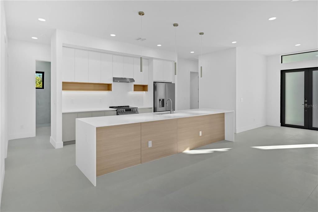 A modern kitchen features white upper cabinets, wood-toned lower island cabinetry, and stainless steel appliances — 10065 MEMPHIS STREET, PORT CHARLOTTE, FL