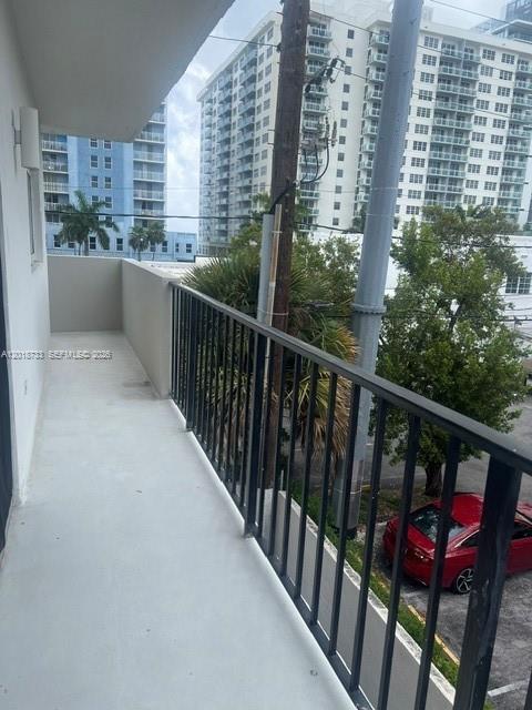 A balcony with a black metal railing overlooks a parking lot and tall apartment buildings — 6965 Harding Ave # 305, Miami Beach FL 33141, MIAMI BEACH, FL